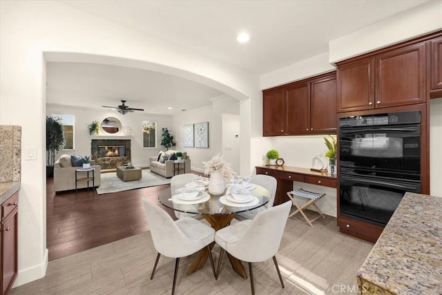 dining area featuring arched walkways, recessed lighting, light wood-style flooring, a ceiling fan, and a glass covered fireplace