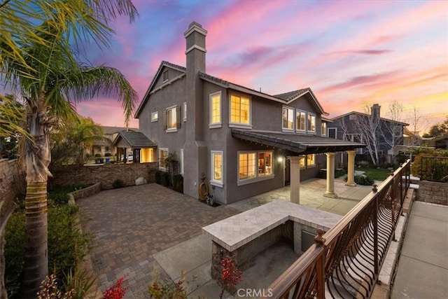 back of property at dusk featuring a patio area, a chimney, and stucco siding