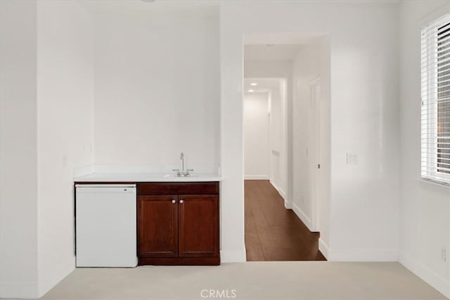 bar with wood finished floors, white dishwasher, a sink, and baseboards