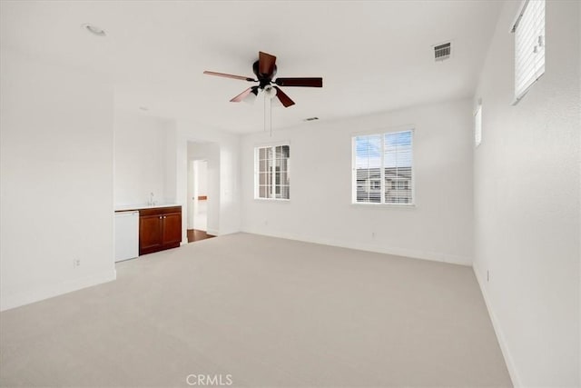 empty room with a ceiling fan, light colored carpet, visible vents, and baseboards