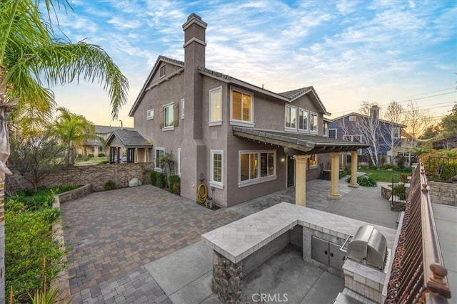 back of property at dusk featuring a patio area, an outdoor kitchen, and stucco siding