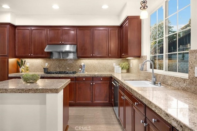 kitchen featuring under cabinet range hood, light countertops, a sink, and hanging light fixtures