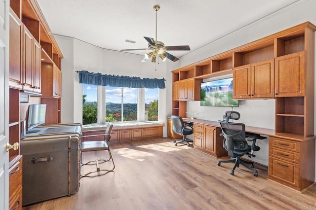 office space with light wood-type flooring, ceiling fan, visible vents, and built in desk