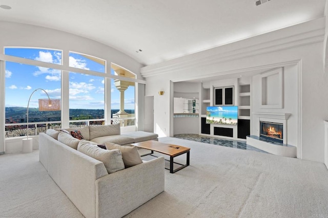 living room featuring built in shelves, lofted ceiling, light colored carpet, a glass covered fireplace, and a mountain view