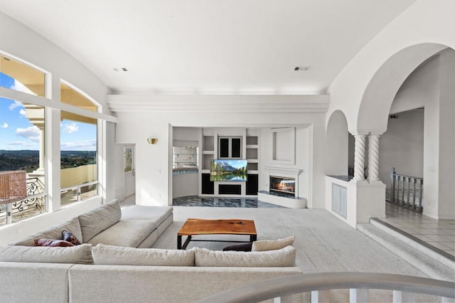 living room featuring arched walkways, built in shelves, a glass covered fireplace, and visible vents