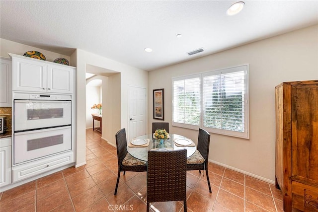 dining area featuring arched walkways, light tile patterned flooring, visible vents, and baseboards