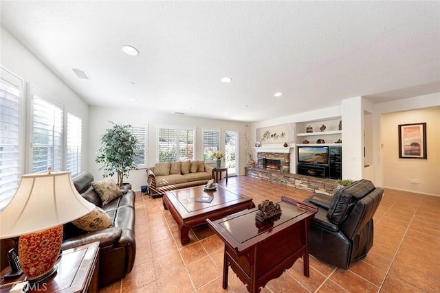 living area featuring a stone fireplace, built in shelves, light tile patterned flooring, and a healthy amount of sunlight