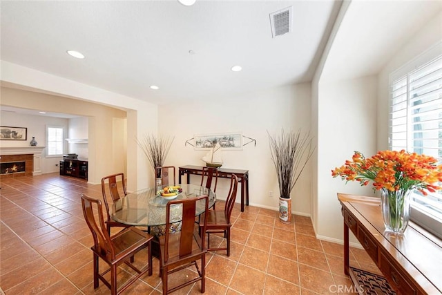 tiled dining area with a warm lit fireplace, baseboards, visible vents, and recessed lighting