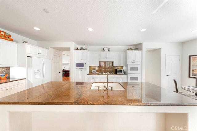 kitchen featuring white appliances, dark stone counters, a spacious island, white cabinetry, and a sink