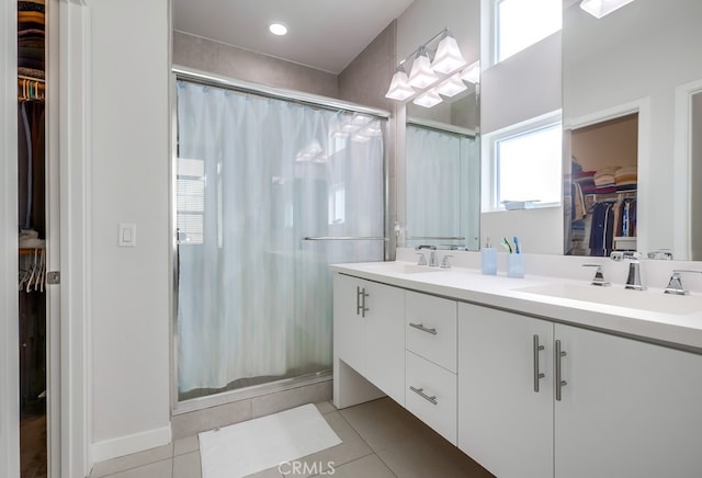 bathroom with double vanity, a spacious closet, a stall shower, a sink, and tile patterned flooring