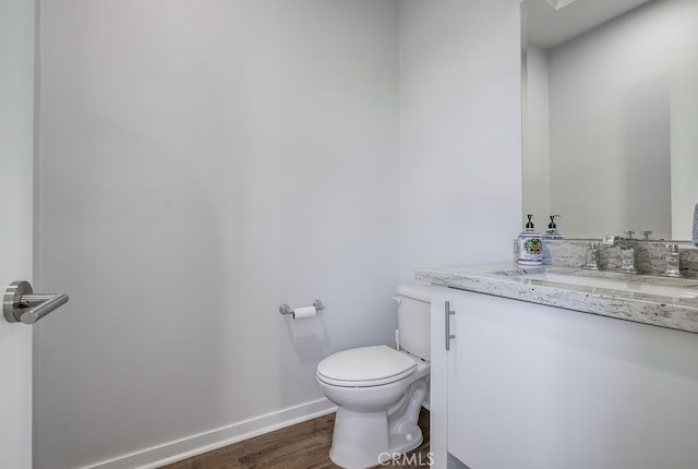 half bath with baseboards, vanity, toilet, and wood finished floors