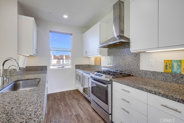 kitchen featuring stainless steel appliances, wall chimney range hood, a sink, and white cabinetry