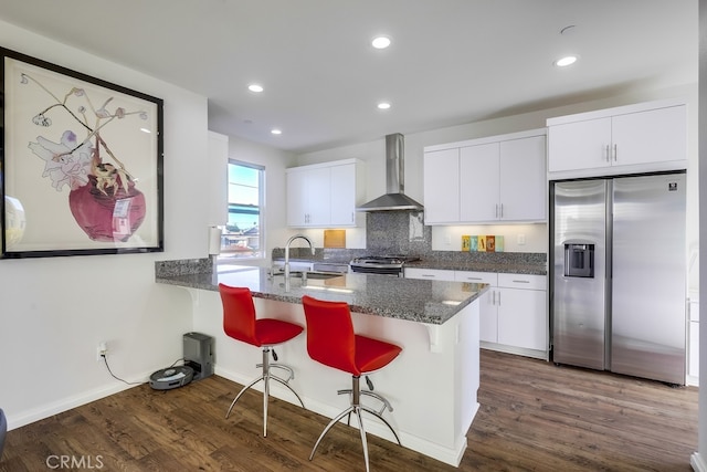 kitchen featuring dark wood-style flooring, a sink, white cabinetry, appliances with stainless steel finishes, and wall chimney range hood