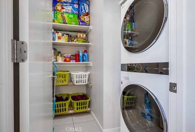 washroom featuring light tile patterned floors, laundry area, stacked washing maching and dryer, and baseboards