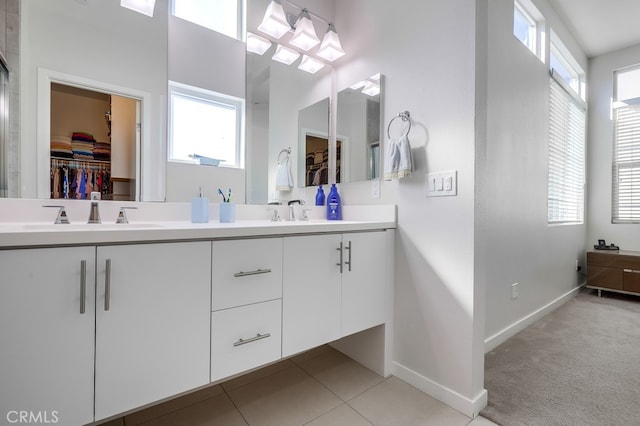 bathroom with a walk in closet, a sink, baseboards, and double vanity