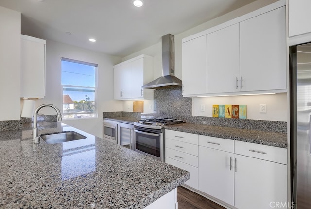 kitchen with stainless steel appliances, white cabinetry, a sink, and wall chimney range hood