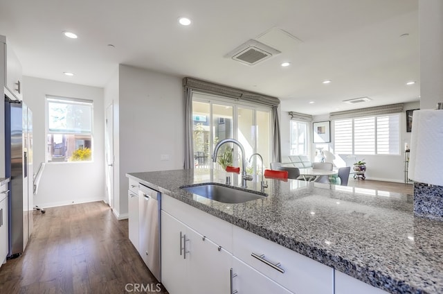 kitchen featuring dark wood finished floors, appliances with stainless steel finishes, white cabinetry, a sink, and dark stone counters