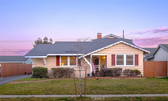 view of front of home featuring roof with shingles, a lawn, a chimney, and fence