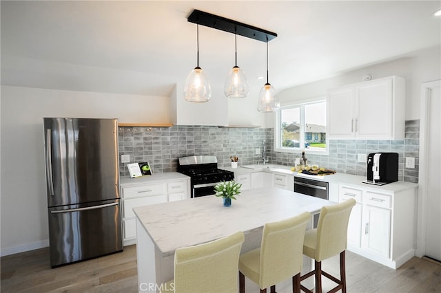 kitchen with a kitchen island, white cabinets, appliances with stainless steel finishes, decorative backsplash, and decorative light fixtures