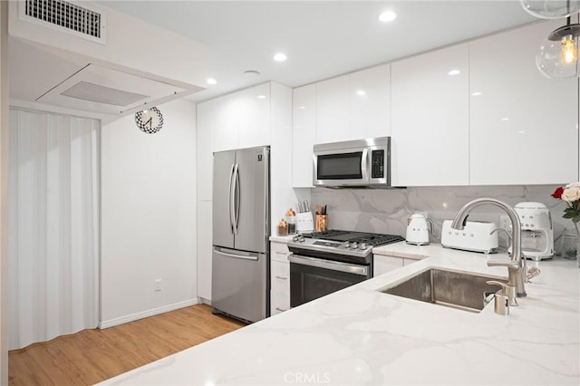 kitchen with modern cabinets, appliances with stainless steel finishes, white cabinets, and light stone counters