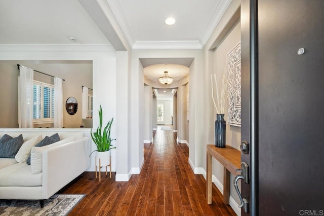 hallway featuring arched walkways, ornamental molding, dark wood-style flooring, and baseboards