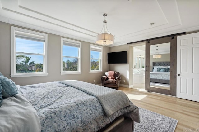 bedroom with baseboards, light wood-style floors, ornamental molding, a tray ceiling, and ensuite bath