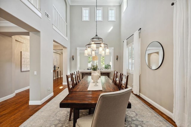 dining space featuring visible vents, a high ceiling, ornamental molding, wood finished floors, and baseboards