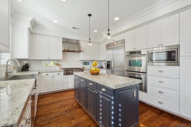 kitchen with visible vents, white cabinets, a sink, built in appliances, and wall chimney exhaust hood