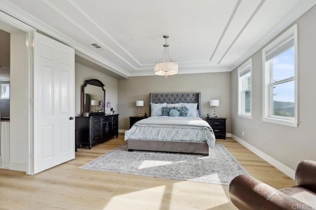 bedroom featuring baseboards, visible vents, ornamental molding, a tray ceiling, and light wood-style floors