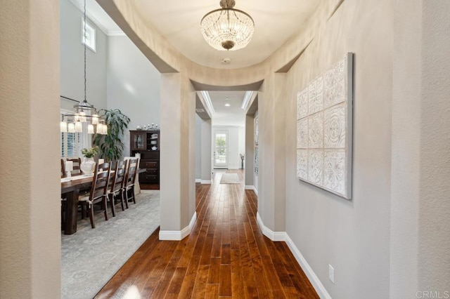 hallway featuring a chandelier, crown molding, baseboards, and wood finished floors