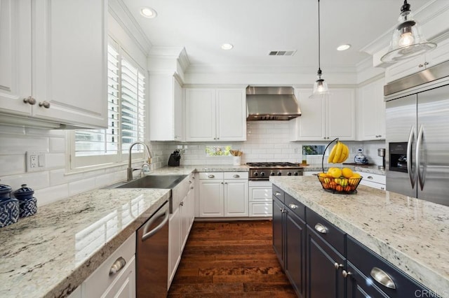 kitchen with wall chimney range hood, appliances with stainless steel finishes, white cabinets, and a sink