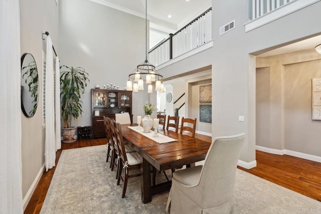 dining space featuring a towering ceiling, wood finished floors, visible vents, and baseboards