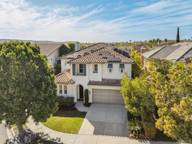 view of front of property featuring a garage, concrete driveway, a tile roof, roof mounted solar panels, and stucco siding