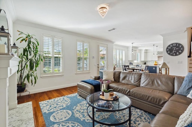 living area with baseboards, wood finished floors, visible vents, and crown molding