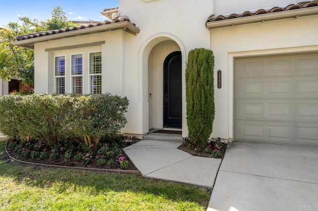 entrance to property featuring an attached garage, stucco siding, and a tiled roof