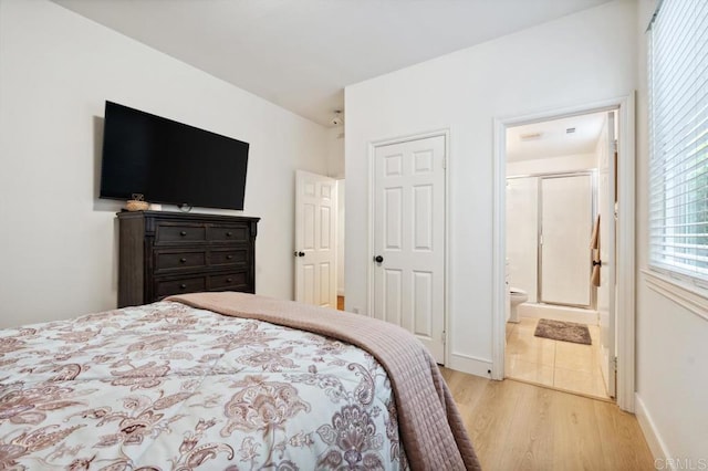 bedroom with light wood-style floors, baseboards, and connected bathroom