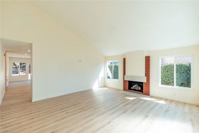 unfurnished living room with light wood-style flooring, a fireplace, high vaulted ceiling, and baseboards