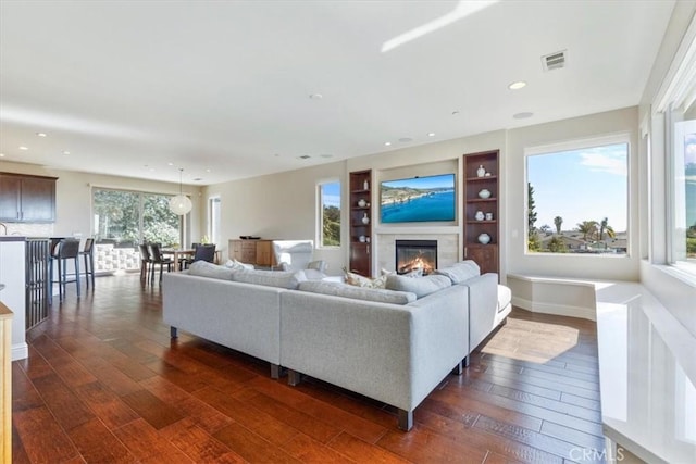 living area with recessed lighting, visible vents, dark wood-type flooring, and a glass covered fireplace