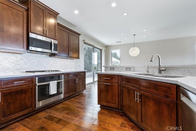 kitchen featuring dark wood finished floors, stainless steel appliances, light countertops, pendant lighting, and a sink