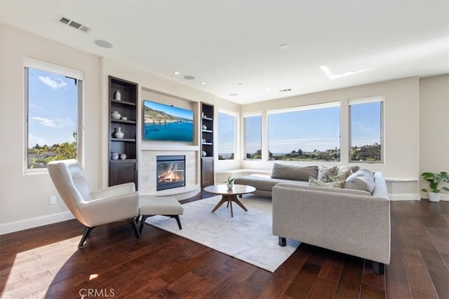 living area featuring built in shelves, visible vents, baseboards, dark wood-style floors, and a glass covered fireplace