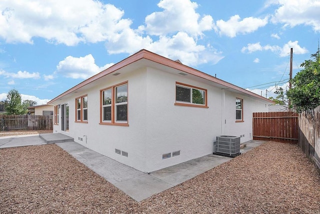 view of side of property with stucco siding, crawl space, a fenced backyard, and central AC unit