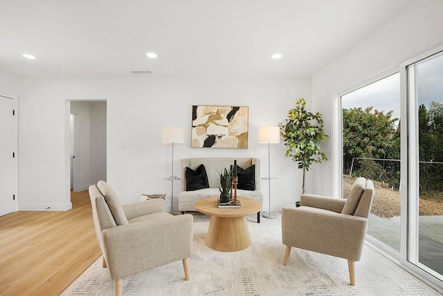 sitting room with a fireplace with raised hearth, wood finished floors, visible vents, and recessed lighting