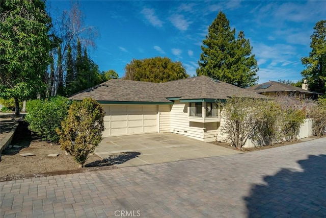 ranch-style home featuring a garage, decorative driveway, and roof with shingles