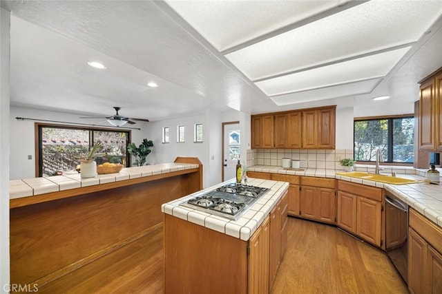 kitchen with a center island, tile counters, appliances with stainless steel finishes, a sink, and light wood-type flooring