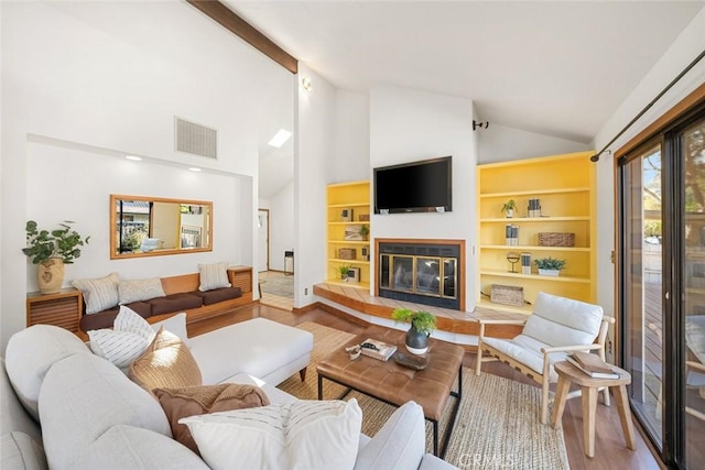 living area with built in features, visible vents, a glass covered fireplace, lofted ceiling, and wood finished floors