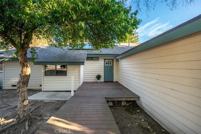 property entrance featuring a deck, roof with shingles, and a patio area