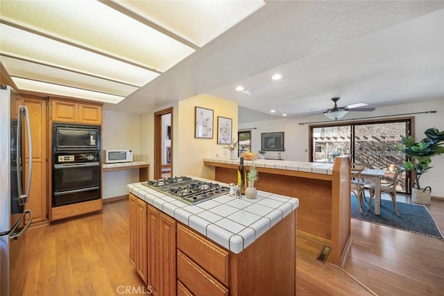 kitchen with tile countertops, black appliances, a kitchen island, and brown cabinetry