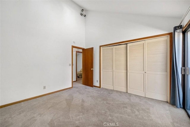 unfurnished bedroom featuring baseboards, high vaulted ceiling, a closet, and light colored carpet