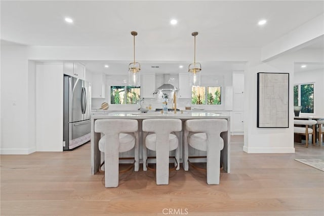 kitchen with white cabinetry, light countertops, freestanding refrigerator, a center island, and wall chimney exhaust hood