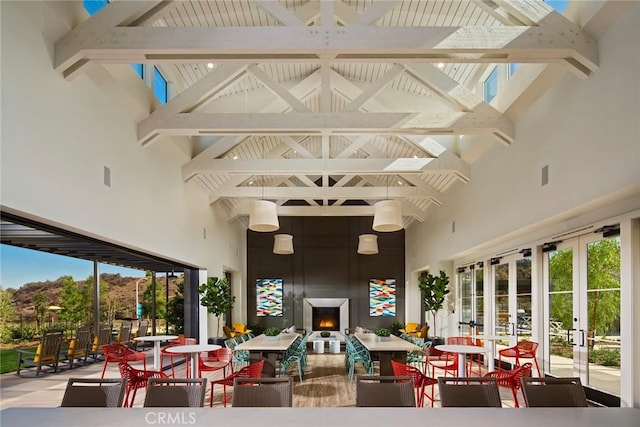 interior space with a warm lit fireplace, french doors, plenty of natural light, and beam ceiling